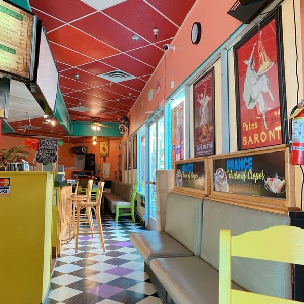 Colorful restaurant interior with checkered floor, red ceiling, booth seating, and French-themed posters.