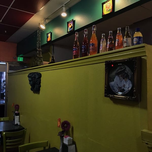 Restaurant interior with lime green walls, dark tables, and decorative bottles and art on a high shelf.