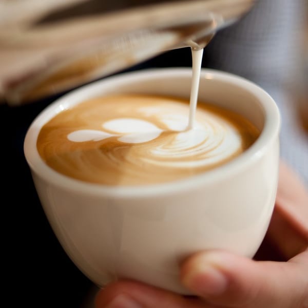Barista pouring milk into a latte, creating a heart-shaped latte art design in a white cup.