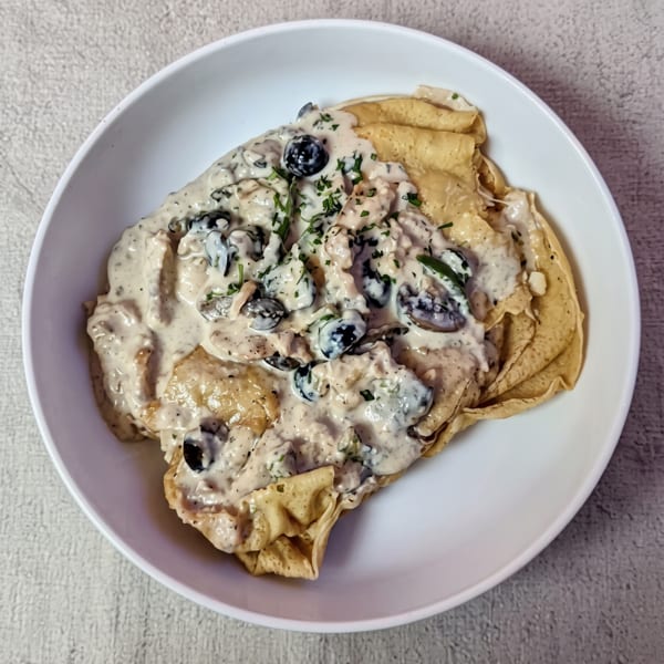 Tortilla chips topped with creamy mushroom sauce, black olives, and chopped herbs on a white plate.