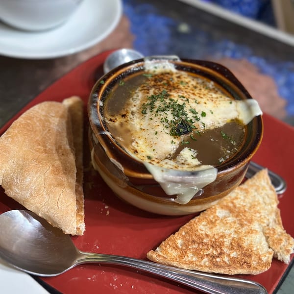 French onion soup with melted cheese and parsley, served with toasted bread on a red plate.