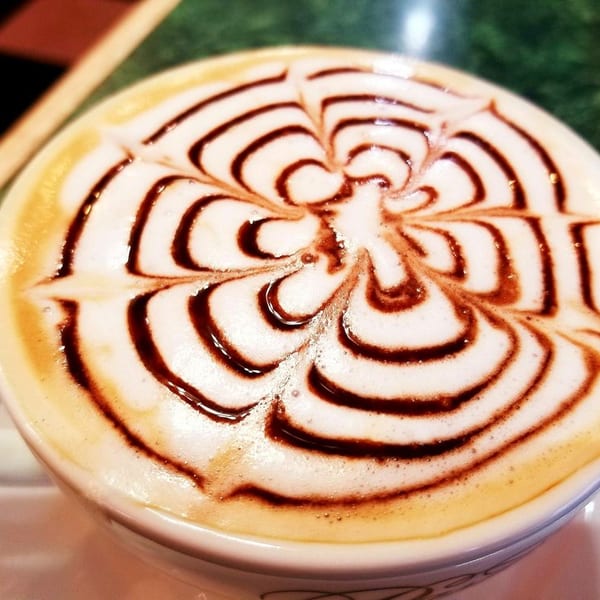 Close-up of a cappuccino with intricate chocolate syrup latte art on foamy milk.