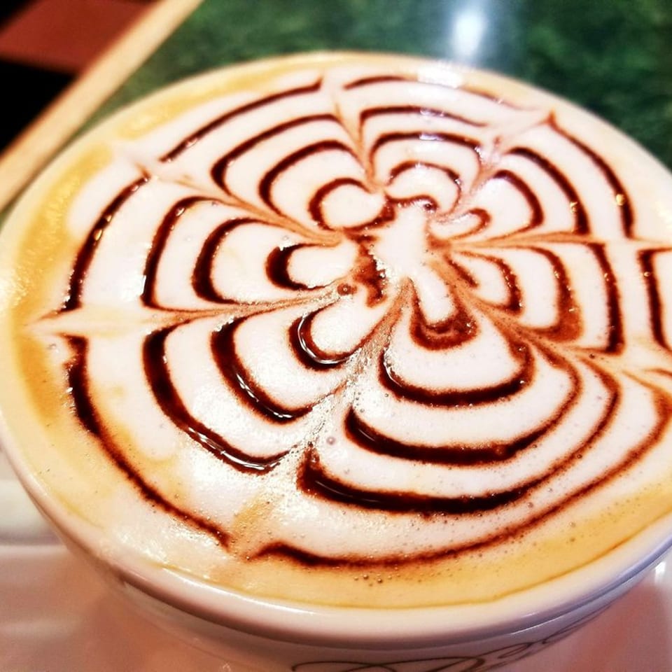 Close-up of a cappuccino with intricate chocolate syrup latte art on foamy milk.