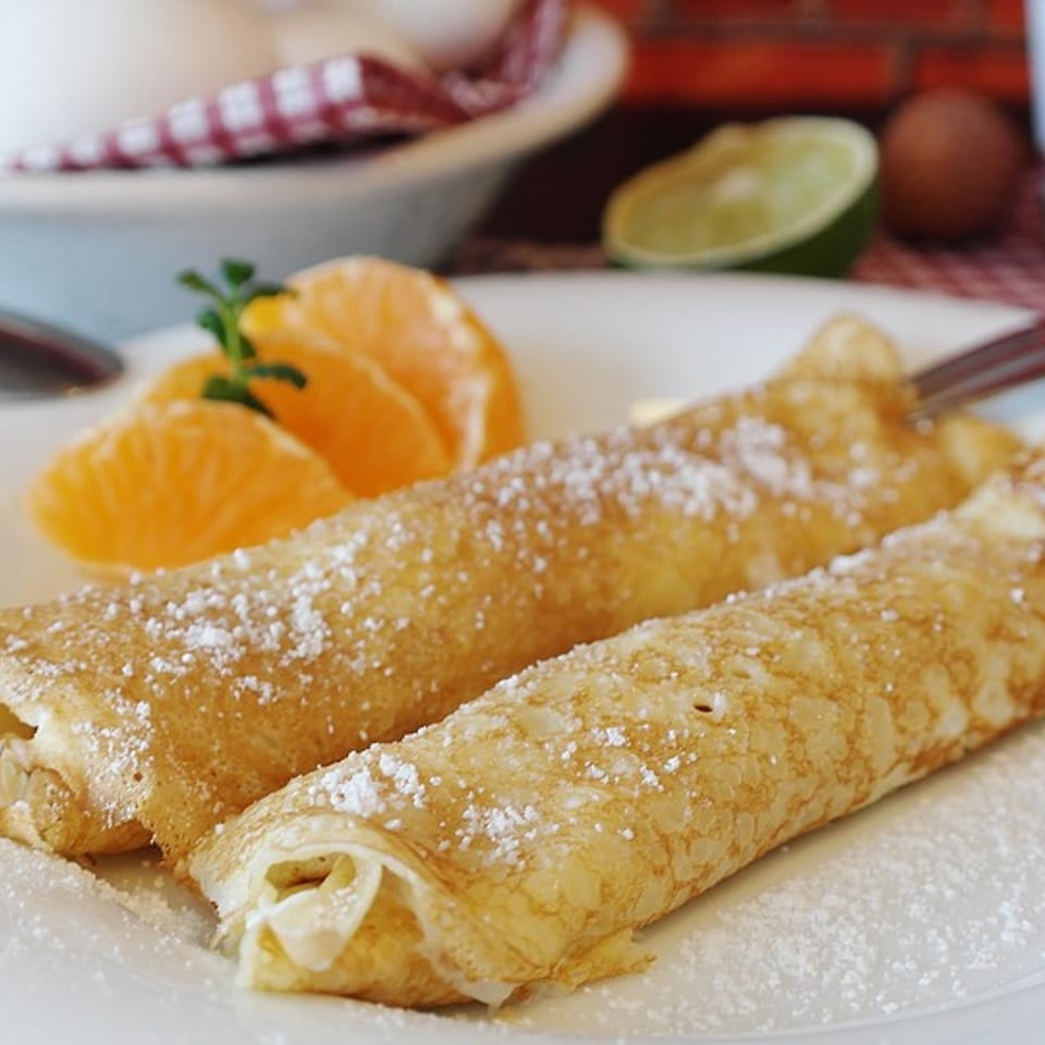Two powdered sugar crepes with orange slices and mint on a white plate.